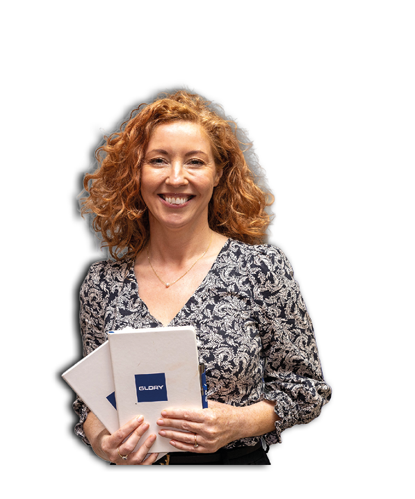 A person with curly hair is smiling and holding two white notebooks with a blue logo on the cover. Description generated by AI