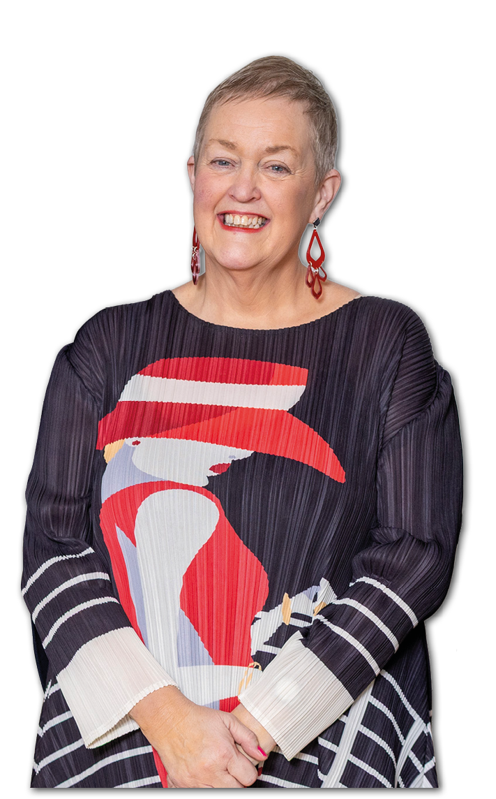 A smiling senior with short hair wears a dark pleated top featuring a bold graphic of a person in a red hat and dress, paired with matching red earrings. Description generated by AI