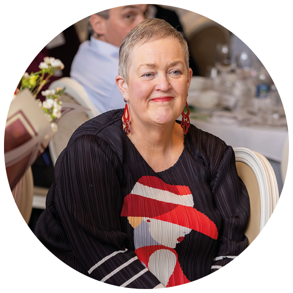 A person with short hair wearing a black top with a red and white design and red earrings is sitting and smiling near a bouquet of flowers. Description generated by AI