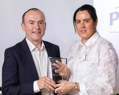 Two adults dressed in formal attire are holding an award together and smiling in a professional setting. Description generated by AI