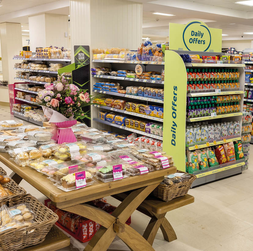 A supermarket aisle displays shelves stocked with various packaged snacks and baked goods under a sign reading Daily Offers. Description generated by AI