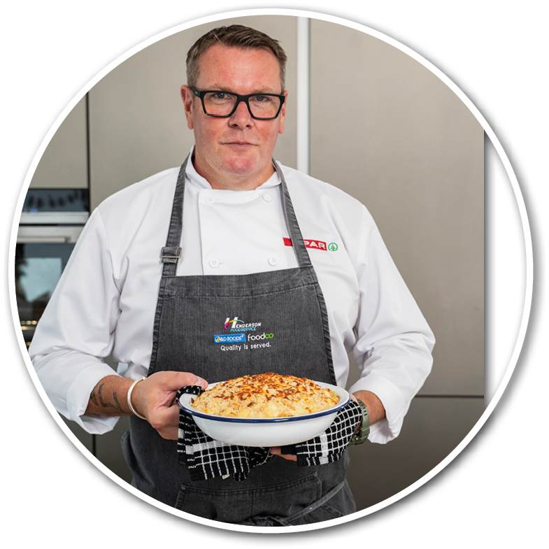 A person wearing glasses and a white shirt with an apron is looking directly at the camera against a plain background. Description generated by AI