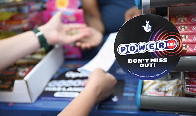 A person is handing money to another person across a counter with a Powerball lottery sign that says “Don't miss out." Description generated by AI
