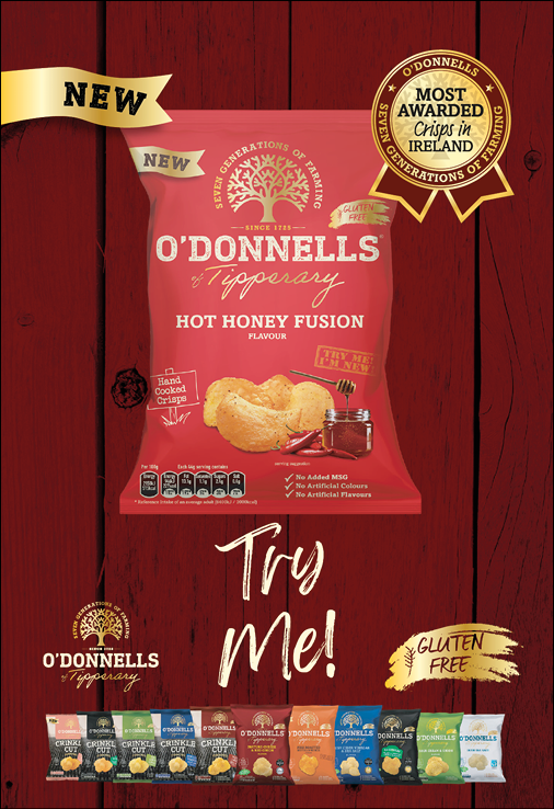 A promotional display features a red bag of O'Donnells Hot Honey Fusion crisps with a gold ribbon highlighting it as new and gluten-free, accompanied by a row of various other O'Donnells crisp flavors and the text “Try Me!" on a wooden background. Description generated by AI