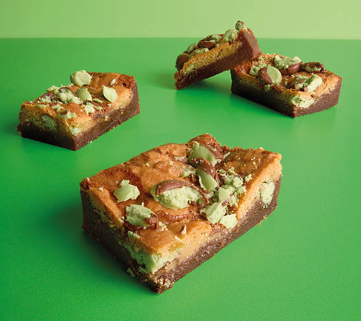 Three rectangular pieces of dessert with a brown crust and greenish topping are arranged on a green surface. Description generated by AI