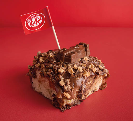 A chocolate dessert topped with chopped nuts, a piece of KitKat chocolate, and a small red flag with the KitKat logo on a red background. Description generated by AI