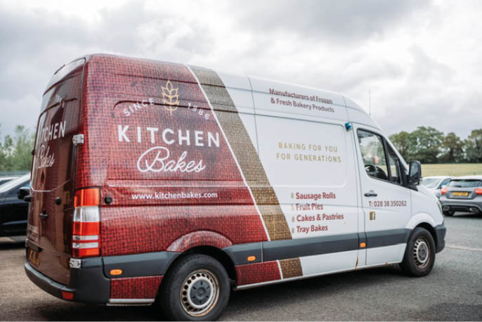 A delivery van parked on a road features branding for Kitchen Bakes, advertising baked goods like sausage rolls, fruit pies, cakes, and pastries. Description generated by AI