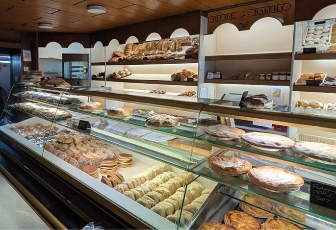 A bakery display case filled with various breads, pastries, and baked goods arranged on shelves and trays under warm lighting. Description generated by AI
