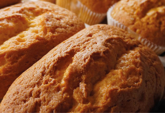 Several freshly baked golden brown muffins are closely arranged on a surface. Description generated by AI