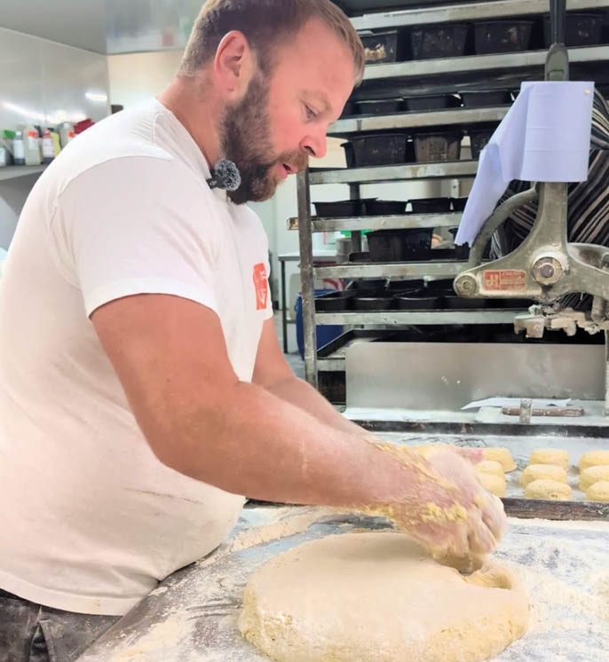 A person wearing a white t-shirt is kneading dough on a floured surface in a kitchen setting. Description generated by AI