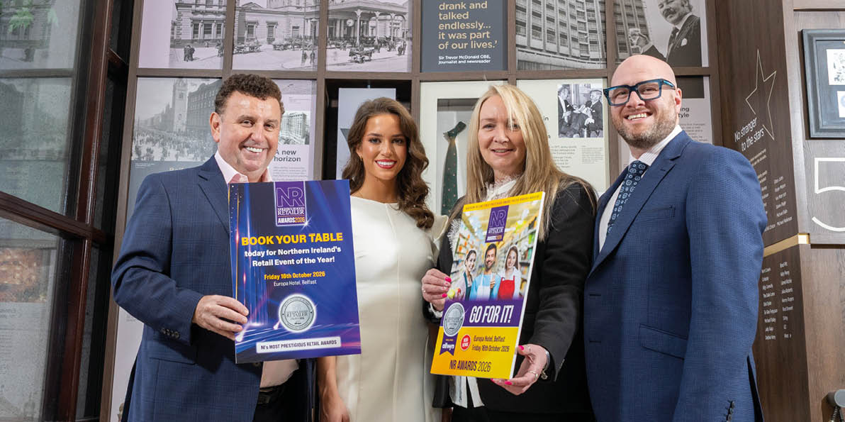 Four adults dressed in business attire stand indoors holding promotional posters in front of a wall with historical photos and a sign that reads Europa Hotel. Description generated by AI