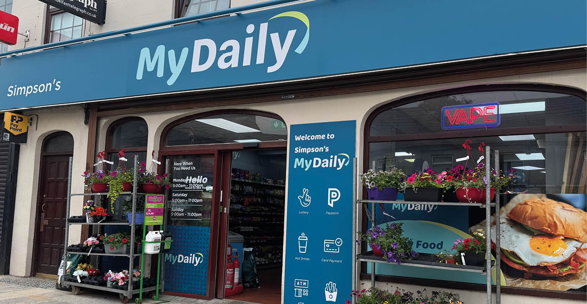 A storefront with a blue sign reading “MyDaily" and flower racks outside displays a neon "OPEN" sign and a large image of a breakfast sandwich in the window. Description generated by AI