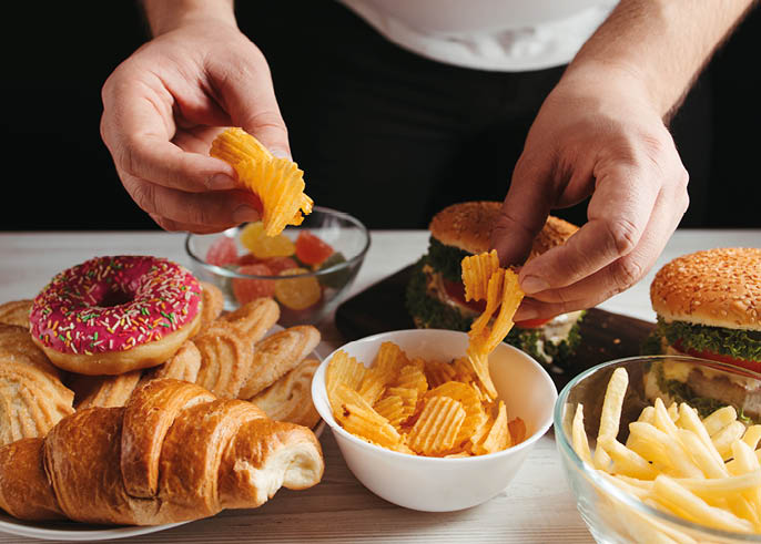 Unhealthy snack, junk food, compulsive overeating. Man overeating unhealthy meals taking hamburger and potato chips from plate