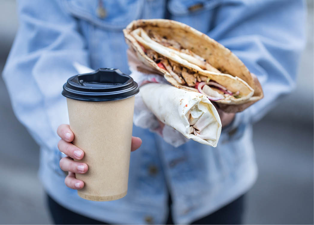 A young woman holding a glass of coffee and fast food. Close up. The concept of fast food .