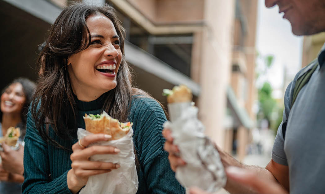 A group of young adults in Sydney share smiles and laughter as they enjoy delicious street food together. The lively atmosphere captures the joy of weekend leisure activities in the city.