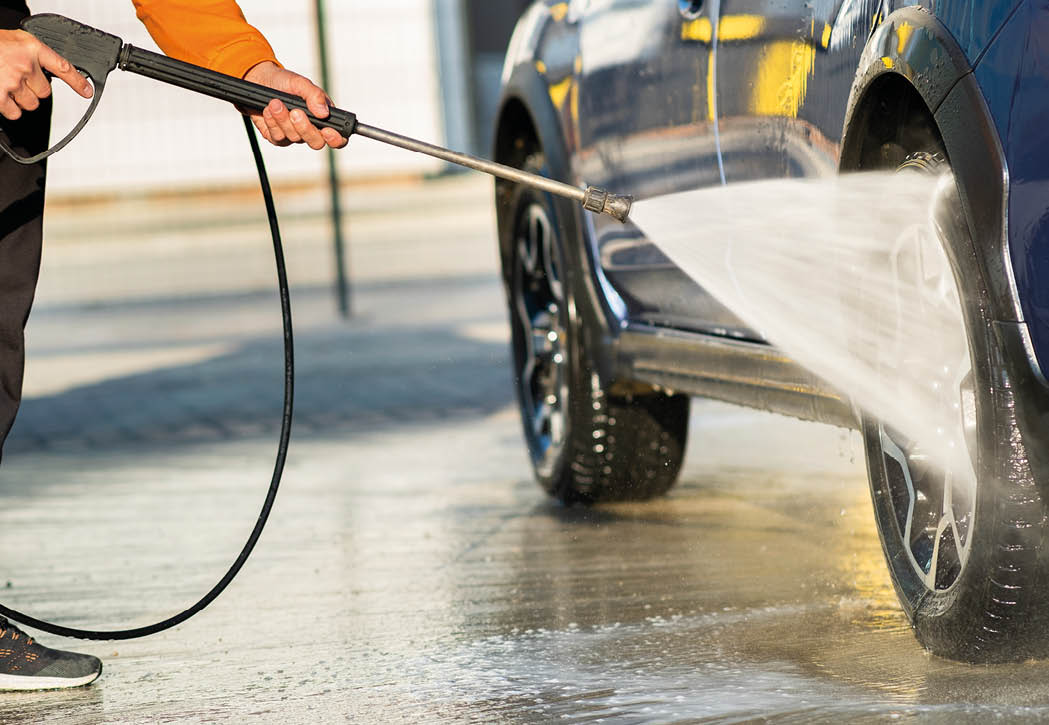 Closeup of male driver washing his car with contactless high pressure water jet in self service car wash.