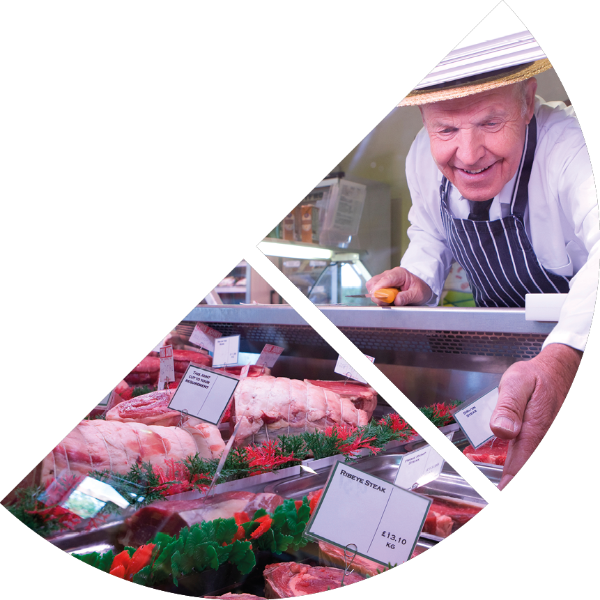 Butcher in apron and hat arranging display of meat in shop chiller