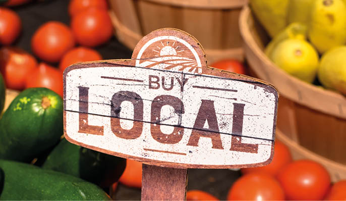 wooden sign with word signage reading buy local produce with tomatoes yellow squash and zucchini background