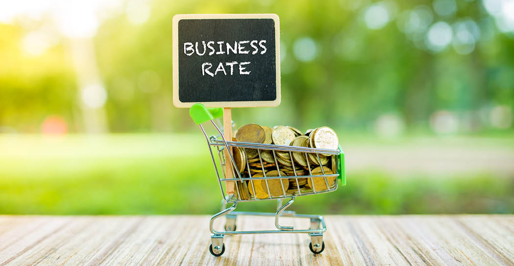 Business Concept : BUSINESS RATE word on black board with coins in small container over blur and sunlight background.