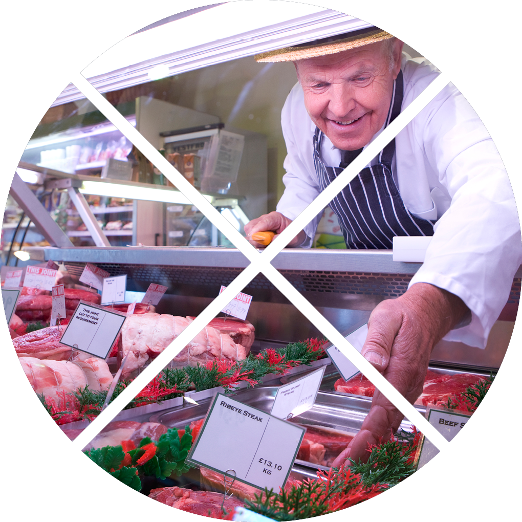 Butcher in apron and hat arranging display of meat in shop chiller