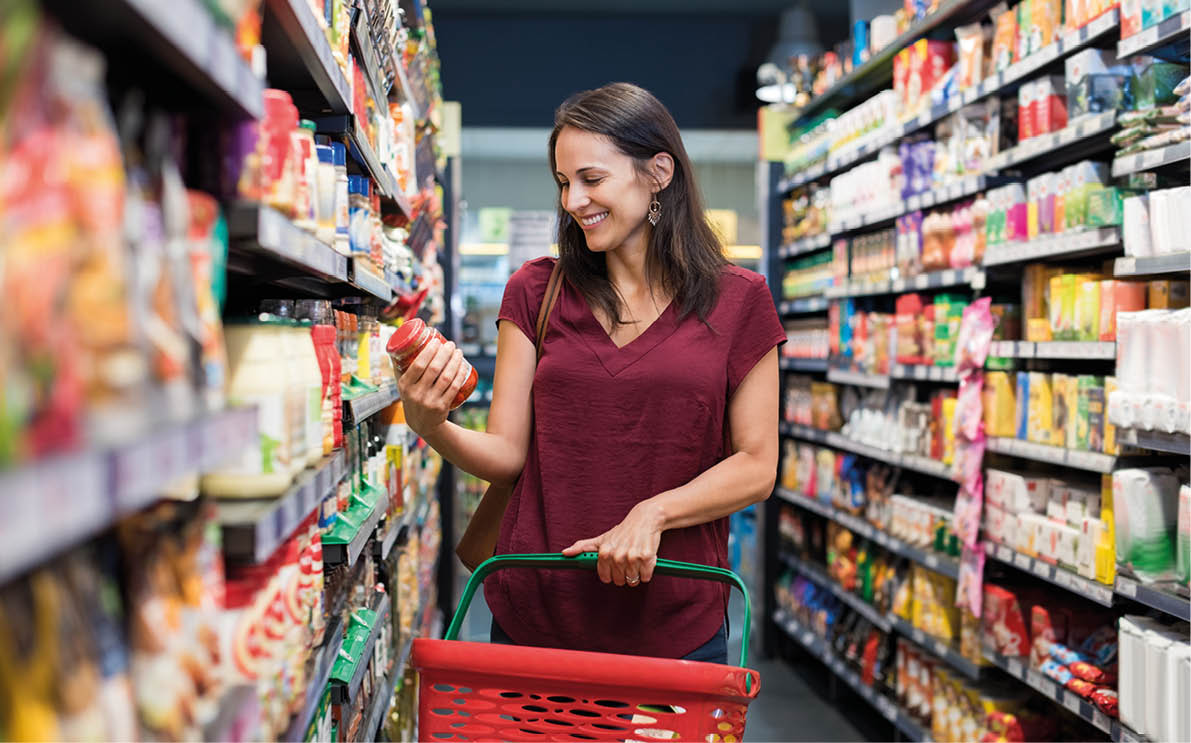 Happy mature woman looking at product at grocery store. Smiling hispanic woman shopping in supermarket and reading product information. Costumer buying food at the market.