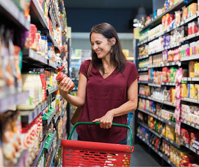 Happy mature woman looking at product at grocery store. Smiling hispanic woman shopping in supermarket and reading product information. Costumer buying food at the market.
