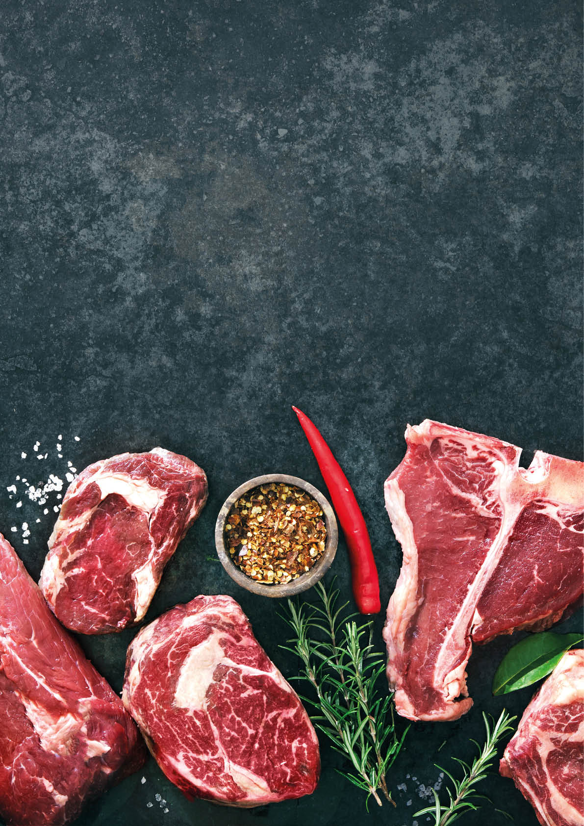 Variety of raw beef meat steaks for grilling with seasoning and utensils on dark rustic board